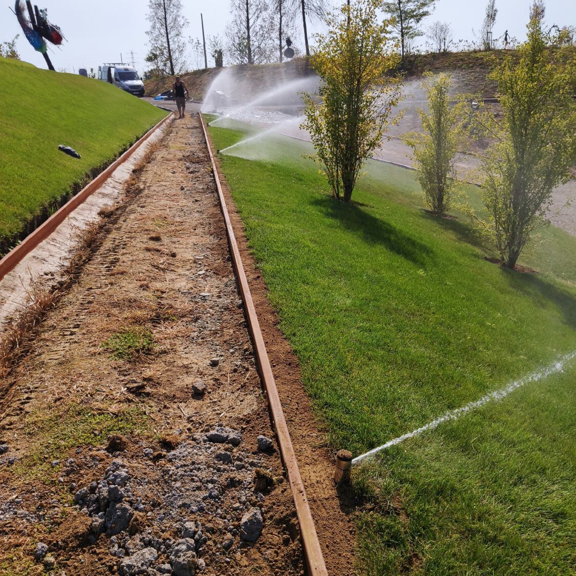 Teren zieleni ze skarpą: Zraszacze rotacyjne na trawniku z nasadzeniami drzew.